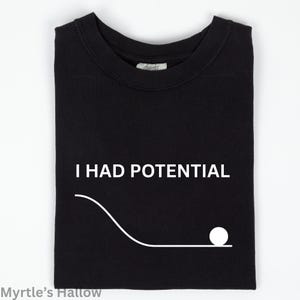 May include: Black t-shirt with the white text "I HAD POTENTIAL" above a white line graphic of a ball rolling down a hill. The shirt is folded and has a tag at the neckline.