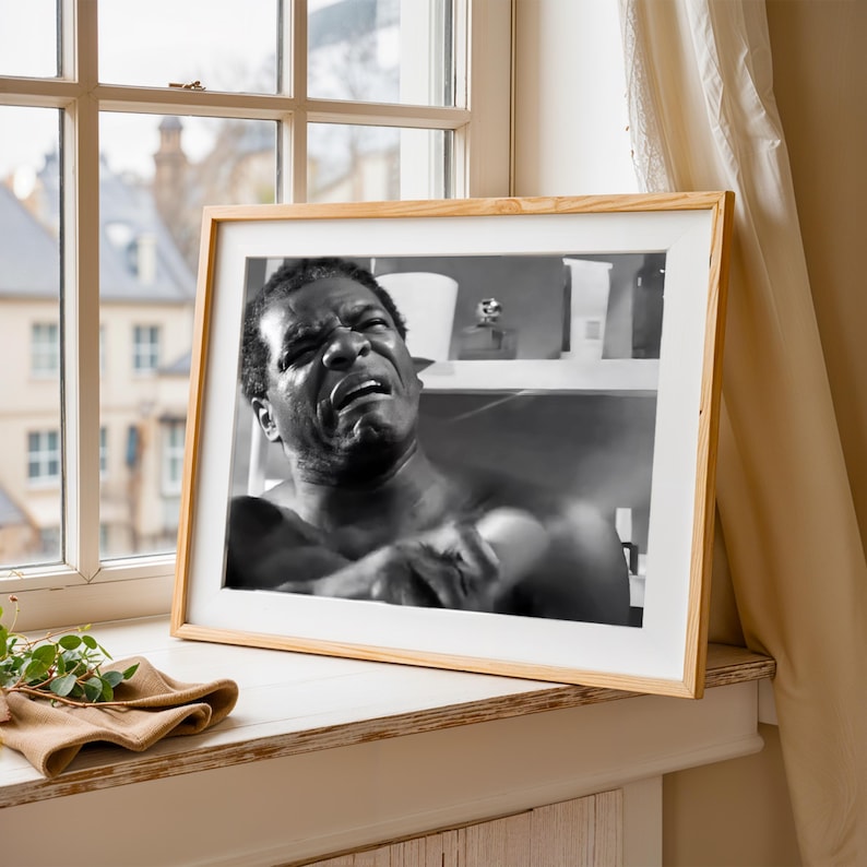a framed black and white photograph of a man with a pained expression, sitting on a windowsill.