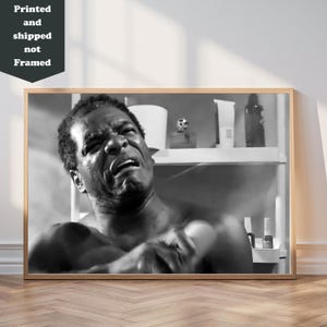 A black and white photograph of a man with a pained expression, sitting on a chair in a bathroom setting.