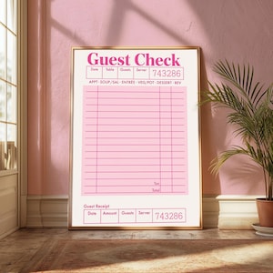 May include: A framed pink and white "Guest Check" print. The print features a receipt design with fields for date, table, guests, and server, along with the number 743286. The words "Guest Check" are in a bold, pink font. The print is displayed in a room with a pink wall.