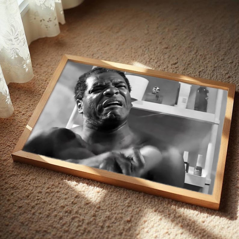 The image is a framed photograph of a man with a serious expression, sitting on a carpeted floor.