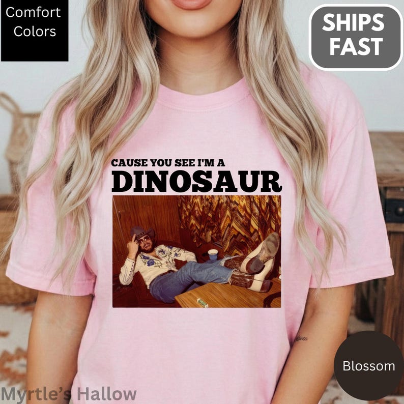 A woman wearing a pink t-shirt with a graphic design featuring a man lying down and the text "CAUSE YOU SEE I'M A DINOSAUR".