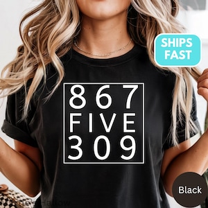 以下が含まれることがあります： 白枠の中に数字の867、FIVE、309がプリントされた黒いTシャツ。テキストは太字のサンセリフ体です。Tシャツは無地の黒色です。クルーネックです。