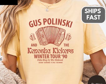 Puede incluir: Camiseta de color mantequilla con un gráfico granate. El diseño presenta el texto "Gus Polinski and The Kenosha Kickers Winter Tour '90", un acordeón y jarras de cerveza. La camiseta es de color cómodo.