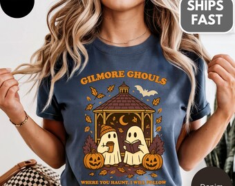 Może przedstawiać: Niebieska koszulka dżinsowa z pomarańczowym napisem "GILMORE GHOULS". Grafika przedstawia dwie postacie duchów, dynie i altanę. Poniżej nadrukowano frazę "WHERE YOU HAUNT, I WILL FOLLOW".