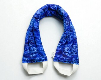 May include: A blue neck wrap with a paisley pattern and white trim. The wrap is made of a soft fabric and is designed to be worn around the neck. The paisley pattern is in shades of blue.