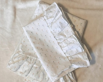 Puede incluir: Juego de cama blanco con estampado floral. El juego incluye una sábana encimera, una sábana bajera y una funda de almohada. Las sábanas tienen un delicado estampado de pequeñas flores en tonos amarillos, grises y azules. La funda de almohada y la sábana superior tienen un borde con volantes.