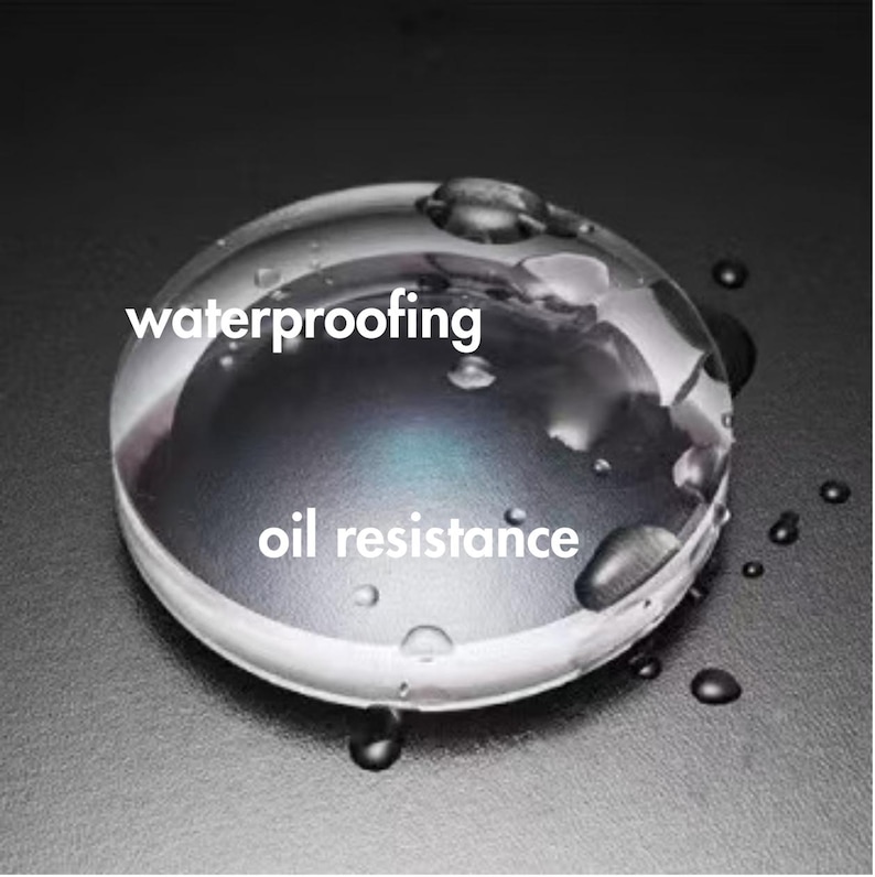 May include: A clear, round lens with water droplets on its surface. The text "waterproofing" and "oil resistance" are displayed in white. The lens is set against a dark gray background.