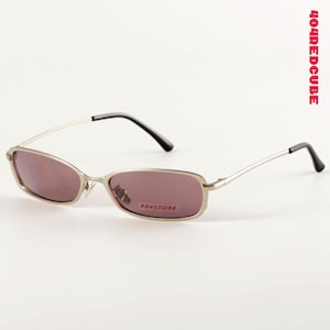 Könnte beinhalten: Sonnenbrille mit silbernem Rahmen und rechteckigen, mauvefarbenen Gläsern. Die Bügel sind silberfarben mit schwarzen Spitzen. Der Text "404STORE" ist auf dem rechten Glas aufgedruckt. Der Text "404REDCUBE" ist vertikal auf der rechten Seite aufgedruckt.