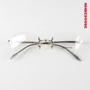 Óculos Bayonetta Y2K com armação oval sem aro, lentes transparentes e estrutura metálica leve.