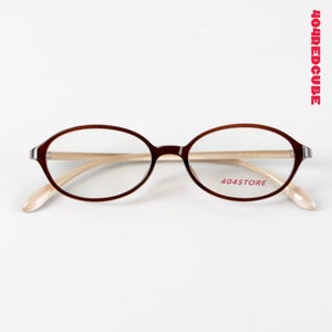 May include: Oval-shaped spectacles with a dark brown frame and light beige temples. The lenses are clear, and the text "404STORE" is printed on the lower right lens. The text "404REDCUBE" is printed vertically on the right side.