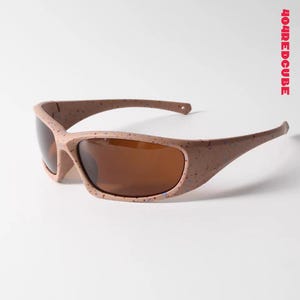 May include: Sport sunglasses with a speckled, light brown frame and brown lenses. The sunglasses have a curved design and are angled slightly to the left. The text "404REDCUBE" is printed vertically in red on the right side.