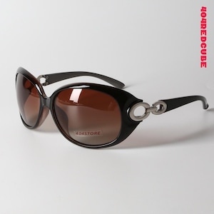 以下が含まれることがあります： 黒い楕円形のサングラス、茶色のグラデーションレンズ付き。 フレームは光沢仕上げで、テンプルにはシルバーカラーの金属製のディテールが施されています。 レンズには「404STORE」の文字が見えます。