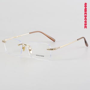 Puede incluir: Gafas sin montura con montura dorada y patillas marrones. Las lentes son rectangulares y llevan el texto "404STORE". La patilla derecha tiene un diseño decorativo.