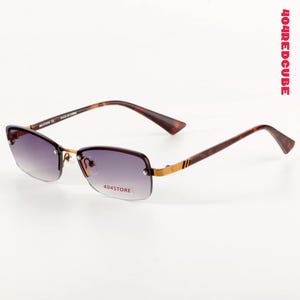 May include: Rimless sunglasses with gradient lenses. The frames are a tortoiseshell pattern with gold accents and the text "404STORE" on the bottom of the lenses. The arms are a dark brown color. The text "404REDCUBE" is on the right side.