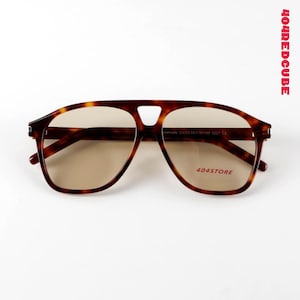 May include: Brown tortoiseshell-patterned sunglasses with a keyhole bridge and light brown lenses. The text "404STORE" is printed on the right lens. The frame has a classic aviator shape.