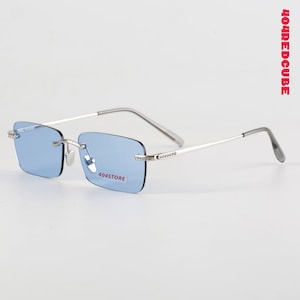 May include: Rimless rectangular sunglasses with light blue lenses and silver frames. The thin temples lead to curved ear pieces. The text "404STORE" is visible on the lens.