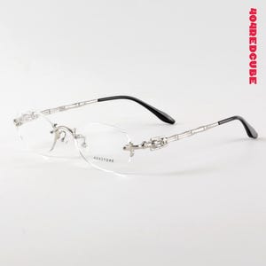 May include: Rimless eyeglasses with clear lenses and silver-toned metal frames. The temples are black and the lenses have the text "404STORE". The text "404REDCUBE" is in the upper right corner.