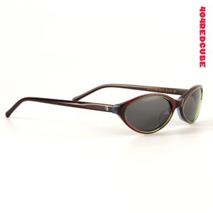 May include: Oval-shaped sunglasses with dark lenses and a burgundy frame. The frame has a green and blue accent around the lenses and dark brown arms. The text "404REDCUBE" is printed vertically in red on the right side.