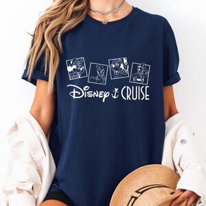 May include: A navy blue t-shirt with a white graphic of four Disney characters in squares and the text "Disney Cruise".