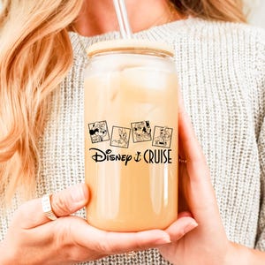 May include: A clear glass tumbler with a wooden lid and a straw. The tumbler has a black and white graphic of Disney characters and the text "Disney Cruise".
