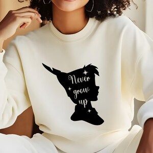 Może przedstawiać: Biała bluza z czarnym siluetem Piotrusia Pana i tekstem "Never grow up".