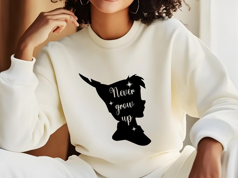 Może przedstawiać: Biała bluza z czarnym siluetem Piotrusia Pana i tekstem "Never grow up".