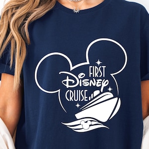 May include: A navy blue t-shirt with a white Mickey Mouse silhouette and the text "First Disney Cruise" inside the ears.