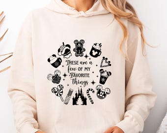 Op de afbeelding: Crèmekleurige hoodie met een cirkelvormig ontwerp van zwart-witte Disney-iconen, waaronder een kasteel en Mickey Mouse-vormige lekkernijen, met de tekst "These are a few of my favorite things."