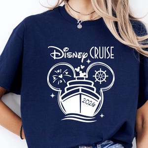 May include: Navy blue t-shirt with a white graphic. The graphic features the words "Disney Cruise" above a ship design with Mickey Mouse ears, a ship's wheel, and the year 2026. The shirt is a casual wear item.