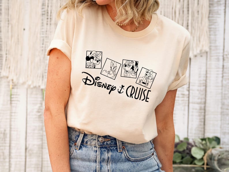 May include: A white t-shirt with a black graphic of Disney characters in picture frames. The text "Disney & Cruise" is below the frames.