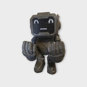 Könnte beinhalten: Graue, 3D-gedruckte Roboterfigur mit einem blockförmigen Kopf und einem bildschirmartigen Gesicht, das einen einfachen Ausdruck zeigt. Der Roboter hat große, geballte Fäuste und steht auf zwei Füßen. Das Design ist minimalistisch und geometrisch.