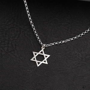 May include: A silver-colored necklace featuring a Star of David pendant. The pendant is a six-pointed star, suspended from a delicate chain. The necklace is displayed against a dark, textured background.