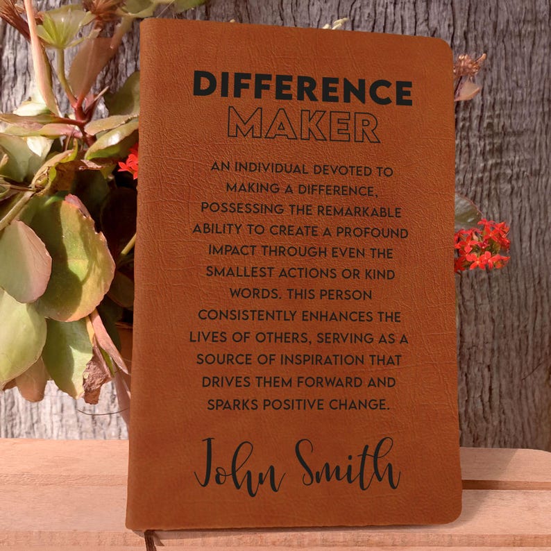 Puede incluir: Un diario de cuero marr&oacute;n con el texto "Difference Maker" y una definici&oacute;n del t&eacute;rmino. El diario est&aacute; personalizado con el nombre "John Smith".