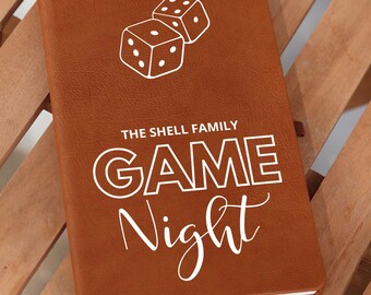 Puede incluir: Un diario de cuero marrón con el texto "THE SHELL FAMILY GAME NIGHT" en letras blancas. Dos dados blancos se representan encima del texto.