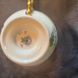 Könnte beinhalten: Weißes Teetassen- und Untertassen-Set mit goldenem Griff. Die Tasse hat ein Blumendesign mit blauen und grünen Akzenten. Der Boden der Tasse trägt den Stempel "C.T. 21 Made in Germany".