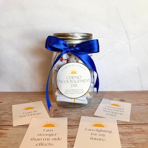 May include: A glass jar filled with rolled-up affirmations, tied with a blue ribbon. The jar has a label that reads "Chemo Encouragement Jar." Four cards with affirmations like "I am stronger" and "I can do hard things" are displayed.