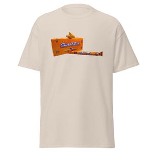 May include: A beige t-shirt with a graphic of a box of Chick-O-Stick cookies and a single cookie stick.