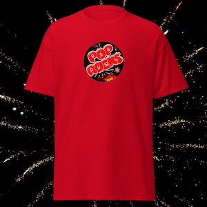 May include: Red t-shirt with a black circle graphic featuring the text "Pop Rocks" in red and white letters with a star and the word "FUN!" in yellow.