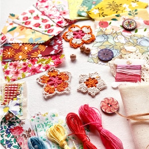 May include: A selection of craft materials featuring floral fabric samples, crochet flower motifs, wooden beads, colourful thread spools, and decorative buttons. The colour scheme includes pink, orange, yellow, and blue.