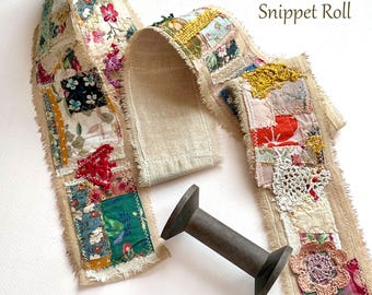 May include: A 40 x 3 inch rustic snippet roll featuring a long strip of beige fabric decorated with various colorful floral and patterned fabric patches, lace, and crochet elements, accompanied by a dark gray wooden spool for winding.