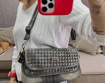 May include: A gray and black crossbody bag with a woven pattern on the flap and a denim-like base. The bag has a long, adjustable strap and gold-colored hardware. The text "22IM YT/12" is visible on the front.