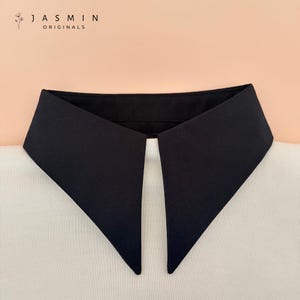 May include: A black detachable collar with a pointed design, set against a white shirt. The collar is a solid black color and is from Jasmin Originals.