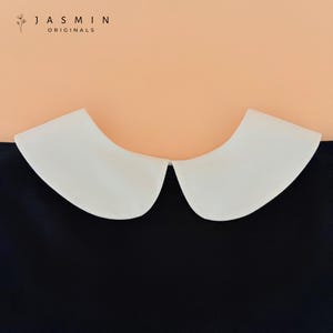 May include: A white Peter Pan collar over a navy blue garment. The collar is a bright white and has a rounded shape. The text "JASMIN ORIGINALS" is in the upper left corner.