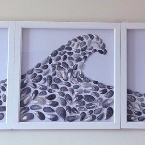 May include: A three-panel artwork depicting a wave. The wave is formed from dark grey seashells, set against a white backdrop within a white framed display. This coastal-themed artwork would make a unique home decor piece.