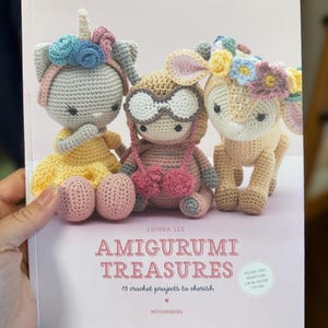 May include: A book titled "Amigurumi Treasures" by Erinna Lee, featuring 15 crochet projects. The cover shows three crocheted amigurumi toys: a unicorn, a pilot, and a deer. The book includes instructions for all crochet stitches.