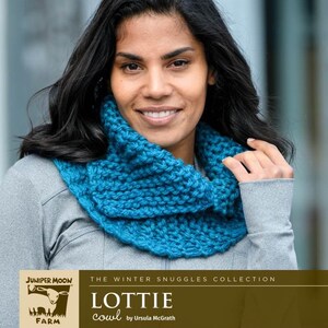 Op de afbeelding: Een vrouw draagt een tealblauwe gebreide col. De col maakt deel uit van de "Winter Snuggles Collection" en is gemaakt met Big Merino Wool. De tekst "Lottie cowl by Ursula McGrath" is zichtbaar. Het Juniper Moon Farm logo is ook zichtbaar.