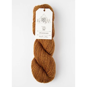 May include: A skein of brown merino wool yarn with a white tag. The tag features the text "RITI" above a mountain and tree design, with the text "100% MERINO WOOL Made in Peru". The yarn is a warm, earthy tone, ideal for knitting and crochet projects.