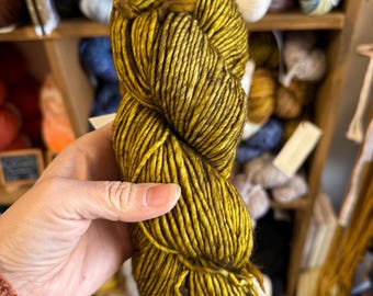 May include: A skein of golden yellow yarn with brown flecks. The yarn is soft and fluffy, and it is perfect for knitting or crocheting.