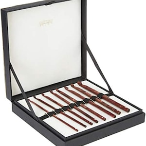 Peut inclure: Un ensemble de crochets dans une boîte noire avec un intérieur blanc. Les crochets sont de couleur brun rougeâtre et sont disposés avec soin dans la boîte. La boîte est ouverte, révélant les crochets. Les crochets sont en bois et ont une finition lisse.